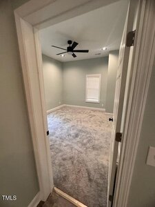 A view through an open doorway into an empty room with light gray carpet, pale green walls, a window with closed blinds, recessed ceiling lights, and a black ceiling fan.