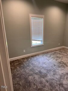 Empty room with light green walls, a single window with white blinds, and gray carpet flooring. Two electrical outlets are visible on the walls. Natural light enters the room through the window.