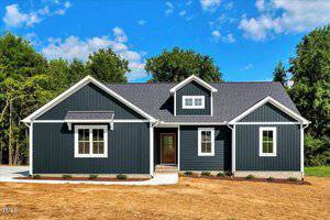 Charming single-story house at 53 Stonewood Loop Lane in Henderson with dark blue vertical siding, white trim, a gray shingle roof, and a cozy front porch. Nestled before woods and clear skies, the yard features minimal landscaping.