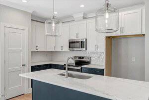 Modern kitchen with white upper cabinets, dark lower cabinets, a marble countertop island with a sink, stainless steel appliances, two glass pendant lights, and an open pantry space.