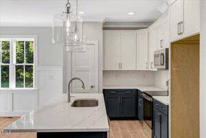 A modern kitchen with white upper cabinets, dark lower cabinets, stainless steel appliances, a built-in microwave, an empty refrigerator space, a center island with a sink, and two pendant lights above.