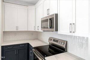 A modern kitchen features white upper cabinets, dark lower cabinets, a stainless steel microwave, an electric stove, and a white geometric tile backsplash with light-colored countertops.