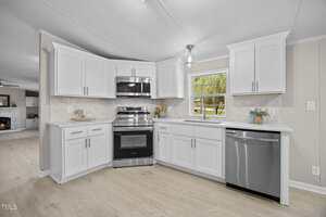 Modern kitchen with white cabinets, stainless steel appliances including a stove, oven, microwave, and dishwasher, light wood flooring, a window above the sink, and neutral-colored walls.