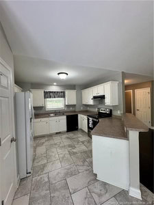 A kitchen with white cabinets, gray countertops, stainless steel appliances, a white refrigerator, a double sink under a window with a black-and-white curtain, and light gray tiled flooring.