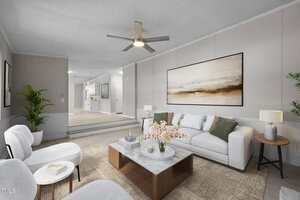 A modern living room with a white sofa, two white chairs, a large abstract painting, a wooden coffee table, and decorative plants. The space leads into a kitchen area with white cabinetry.