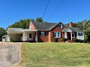 A single-story red brick house with white siding accents at 43 Church Street, Oxford, features black shingles and a covered carport on the left. The home sits on a grassy lawn under a clear blue sky.
