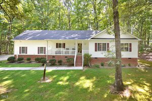 Charming single-story house in Franklinton with white siding and red brick foundation, front porch with white railing, gable roof, brown shutters, surrounded by trees, and a grassy yard at 4056 Ridgeway Drive.