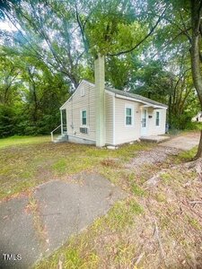 A small, single-story beige house with white trim sits on a grassy lot at 632 Breckenridge Street in Henderson, surrounded by tall trees. A short set of steps leads to the front door, with a concrete walkway in the foreground.