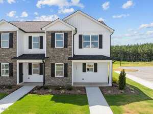 A two-story townhouse at 1106 Brookrun Drive, Oxford, features stone and white siding, black shutters, and a covered front porch. The landscaped yard includes grass and small shrubs, with a driveway visible on the right.