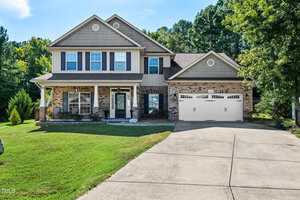 Charming two-story suburban house at 1174 Jackson Court in Creedmoor, featuring a brick and siding exterior, attached two-car garage, covered front porch, wide driveway, and a neatly trimmed lawn with trees and shrubs.
