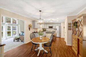 A kitchen and dining area with wood floors, a round table with four chairs, stainless steel appliances, gray cabinets, and a sitting room with large windows in the background.