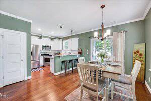 A kitchen and dining area with green walls, white cabinets, stainless steel appliances, a dining table set for four, pendant and chandelier lighting, and a glass door leading outside.