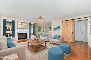 A living room with beige walls, hardwood floor, blue and beige furniture, a rug, a coffee table, a fireplace, ceiling fans, and a wooden sliding barn door leading to another room.