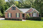 A single-story red brick house with white trim and black shutters sits at 2030 Lonesome Dove Drive in Franklinton, featuring a front porch, green lawn, mature trees, and a driveway on the left.