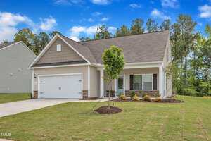 A modern single-story house on 1022 Rhino Bend, Oxford, with gray siding, a two-car garage, and a covered front porch. The fresh sod yard features a small tree and mulched landscaping, framed by trees and a blue sky in the background.