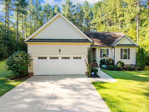 Located at 2122 Turquoise Lane in Franklinton, this single-story house features white siding, a two-car garage, front steps to a small porch, and a well-maintained lawn surrounded by trees and greenery under a clear sky.