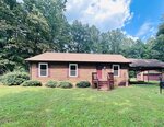 A single-story wooden house with brown siding and a front porch sits on a grassy lawn at 1545 Dogwood Drive, Oxford. Surrounded by trees, it features a small structure and covered area to the right. The sky is partly cloudy.