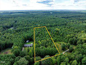 Aerial view of a wooded area in Henderson with a 1.52 Acre Jordan Lane plot outlined in yellow, dense trees throughout, and a house near the bottom left corner, all surrounded by lush forest and greenery.