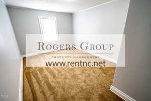 Empty room with white walls, a beige carpet, and a single window letting in natural light. Large watermark text in the center reads "Rogers Group Property Management www.rentnc.net".