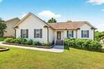 Charming single-story white house at 317 Wick Road, Stem, with a brown shingle roof, gray shutters, front steps, and a landscaped yard. A concrete walkway curves along the well-maintained lawn with shrubs and flowers near the house.