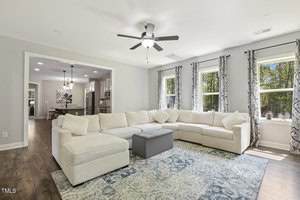 A spacious living room with a large white sectional sofa, a patterned blue rug, and three windows with patterned curtains. The room opens into a dining area and kitchen, with hardwood floors throughout.
