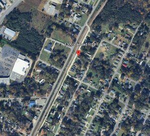 A satellite view showing a neighborhood with houses, a railroad, and a commercial building. A red location pin marks 1300 Railroad Rd near the center of the image. Roads and trees surround the area.