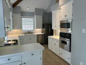 A kitchen with white cabinets, a black refrigerator, a built-in microwave and oven, an electric stovetop, a sink under a window with blinds, and a dishwasher, all set on a neutral tile floor.