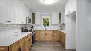 Modern kitchen with white upper cabinets, light wood lower cabinets, stainless steel appliances, white subway tile backsplash, a window above the sink, and light wood flooring.