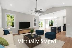 A bright, modern living room at 53 Stonewood Loop Lane, Henderson features a sofa, ottomans, coffee table, TV, and open kitchen. Large windows let in natural light. The words "Virtually Staged" are written across the image.