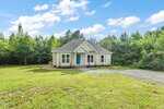 Charming single-story home at 5148 Lucy Averette Road with a gray roof, teal front door, and cozy porch, set on a large grassy lot with a gravel driveway, surrounded by dense trees under a blue sky.