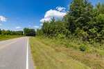 A two-lane rural road in Kittrell curves gently left, bordered by grassy shoulders and dense green trees under a bright blue sky with scattered clouds, near #2 Julie Mcknight Road.