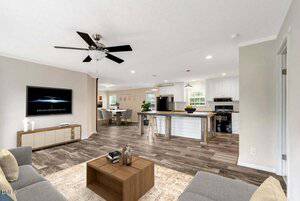 Open-concept living room and kitchen with wood-look flooring, neutral walls, a ceiling fan, a wall-mounted TV, and modern furniture. Kitchen features white cabinets, a center island, and stainless steel appliances.