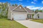 A beige single-story Oxford home at 1017 Rhino Bend features a gable roof, white garage door, and paved driveway. The front yard boasts newly planted grass, small shrubs, and mature trees with a neighboring house in the background.