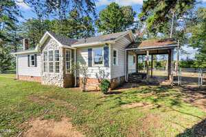 A single-story house at 4193 Ji Oakes Road with white siding, brick foundation, and a stone accent around arched windows; an attached covered porch with steps and a fenced yard, surrounded by trees in Bullock.