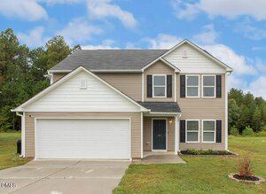 Charming two-story suburban house at 387 Waterfall Road, Henderson, with beige siding, white trim, a double garage, and dark shutters. The home sits on a grassy lawn with a concrete driveway amid trees under a partly cloudy sky.
