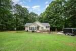 A single-story beige house with white trim sits in a large grassy yard at 2488 Patton Lane, Franklinton. Surrounded by tall trees, it features a wooden ramp to the front door and a black trailer parked on the right side.