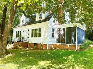A white two-story house at 330 W Young Avenue, Henderson, features a screened porch and red brick foundation on a grassy yard shaded by large trees. Multiple windows and a small porch with steps and railing frame the welcoming front entrance.