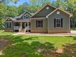 A charming single-story house at 5300 Langdon Drive, Oxford, with gray siding, white trim, black shutters, and a brick foundation. Enjoy the covered front porch surrounded by trees and lush green grass.