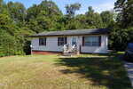 Single-story house at 179 Lynnbank Estates Road in Kittrell, featuring beige siding, a black roof, and a small front porch with steps; surrounded by grass lawn and trees, with a car partially visible on the right side.