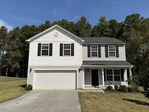 Charming two-story suburban house at 62 W Boulder Road, Henderson, with white siding, black shutters, a double garage, and a covered front porch. Enjoy a grassy yard and trees in the background under a clear sky.