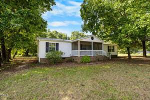 A single-story white house with black shutters and a covered front porch sits at 2080 Thad Carey Road in Oxford, surrounded by trees on a grassy lot under a blue sky with some clouds.