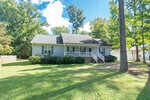 Charming single-story house at 159 Dorsey Pl Place, Henderson, with gray siding, dark roof, a covered front porch with white railings, and steps leading to the yard. Surrounded by trees and shrubbery on a sunny day.