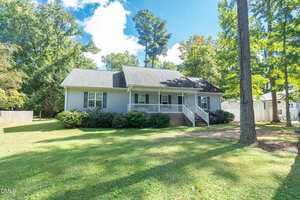 Charming single-story house at 159 Dorsey Pl Place, Henderson, with gray siding, dark roof, a covered front porch with white railings, and steps leading to the yard. Surrounded by trees and shrubbery on a sunny day.