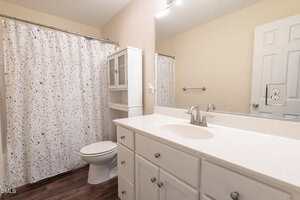 A bathroom with a white vanity and sink, a silver faucet, a large mirror, a toilet, white storage cabinet, wood floor, and a bathtub with a white shower curtain featuring a multicolored dot pattern.