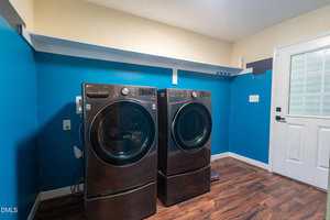 A laundry room with a front-load washer and dryer set on matching pedestals, blue walls, wood-look flooring, a white door with a window, and a white shelf above the machines.