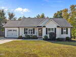 Charming single-story house in Stem at 415 Angus Place with white siding, black shutters, an attached garage on the left, a covered front porch with chairs, trimmed bushes, and a well-maintained front lawn under a partly cloudy sky.