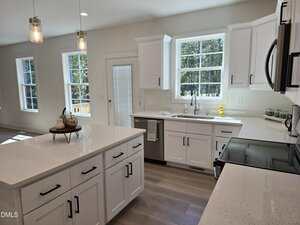 Bright modern kitchen with white cabinets, stainless steel appliances, a large island, quartz countertops, pendant lighting, and multiple windows letting in natural light. A small tray with decor is on the island.