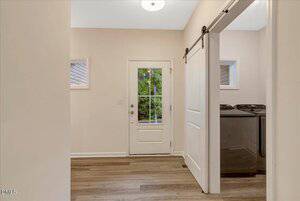 A small mudroom with light-colored walls and wood flooring, featuring a glass-paneled exterior door. A sliding barn door leads to a laundry room with visible washer and dryer units.