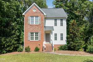 This two-story house at 4106 Geneva Drive in Franklinton features a red brick facade on the left, white siding on the right, gray shutters, a gray front door, a small porch with steps, and attractive landscaping with bushes and trees.