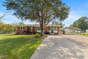 Charming single-story brick house at 936 Eaton Street, Henderson, with a covered front porch, large tree in the front yard, concrete driveway to a carport on the right, and a well-maintained lawn under a clear blue sky.